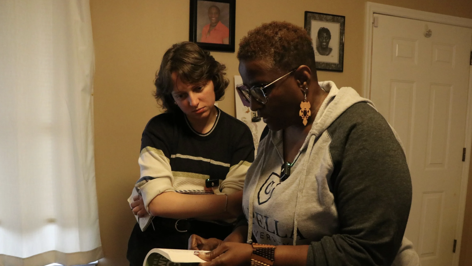 Woman looking over the should of another woman at a book in her home